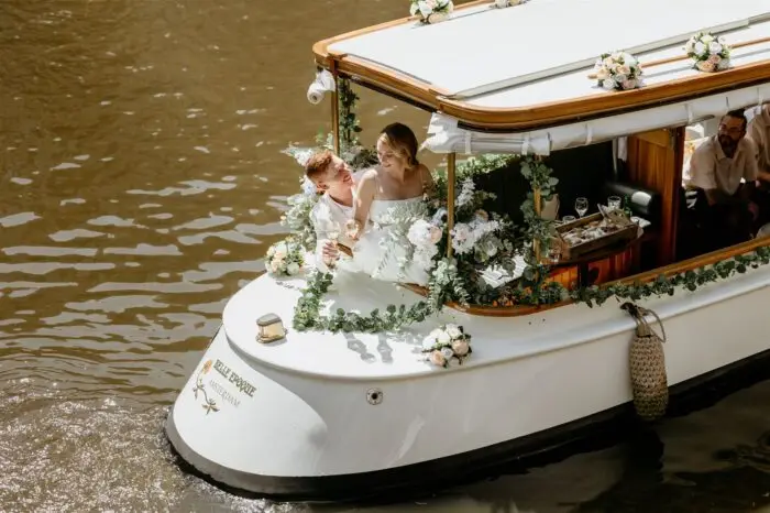 Couple celebrating on a decorated canal boat during an Amsterdam elopement with flowers and drinks