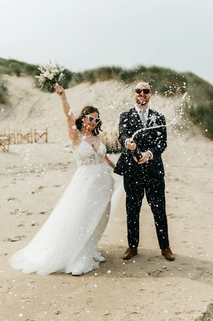 Couple celebrating on the beach after their elopement near Amsterdam with champagne spray