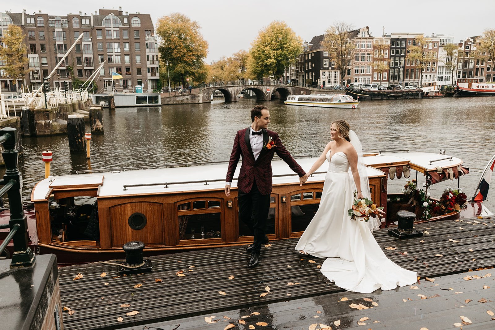 Couple walking along a pier beside their boat during a wedding in Amsterdam with canal views in the background