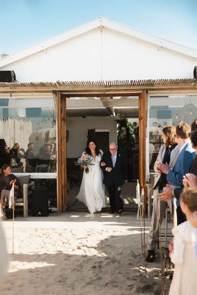 Bride walking onto the beach with guests during a beach wedding ceremony near Amsterdam