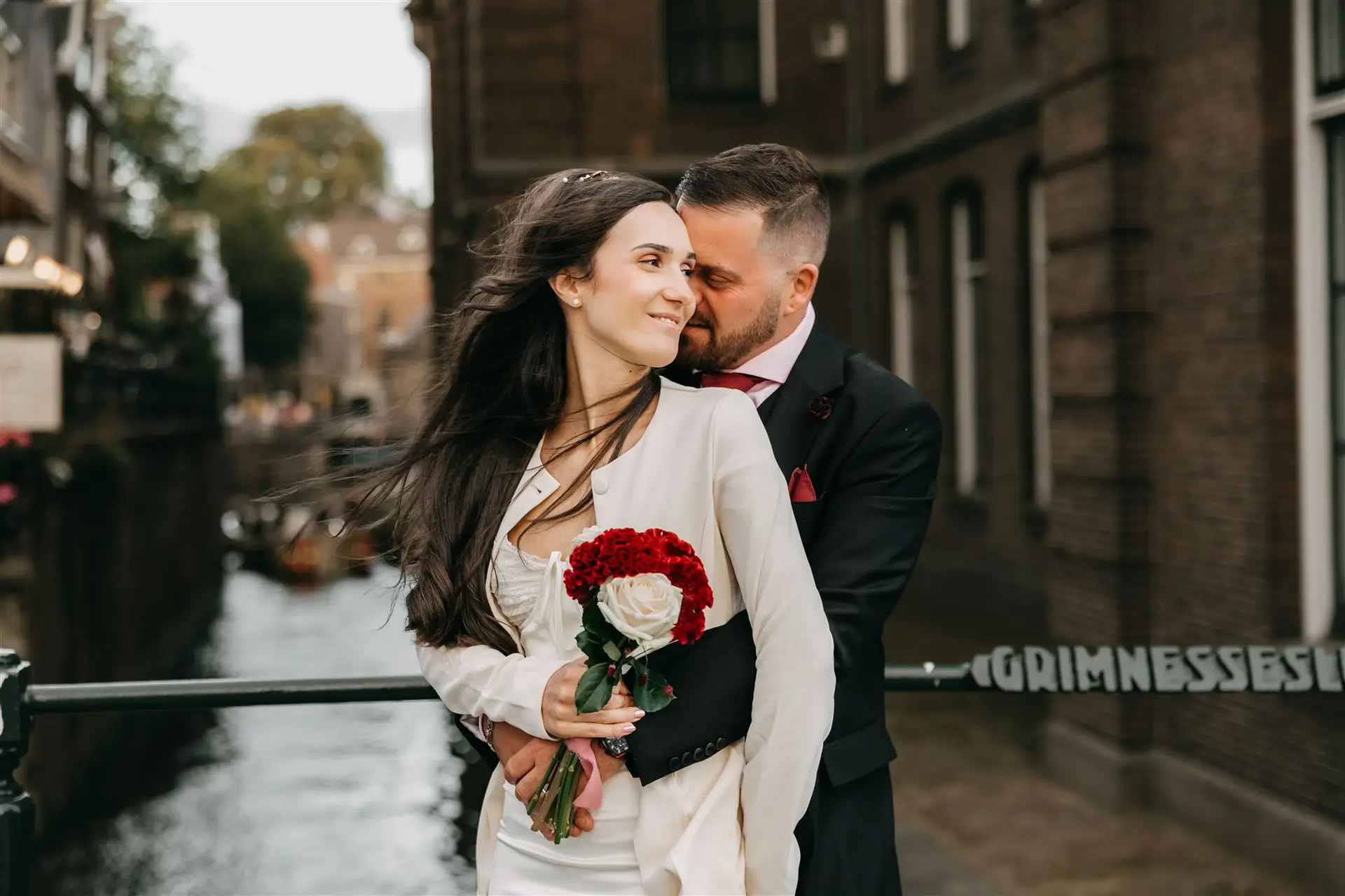 Couple embracing during an Amsterdam elopement photoshoot near a canal with bridal bouquet and historic buildings