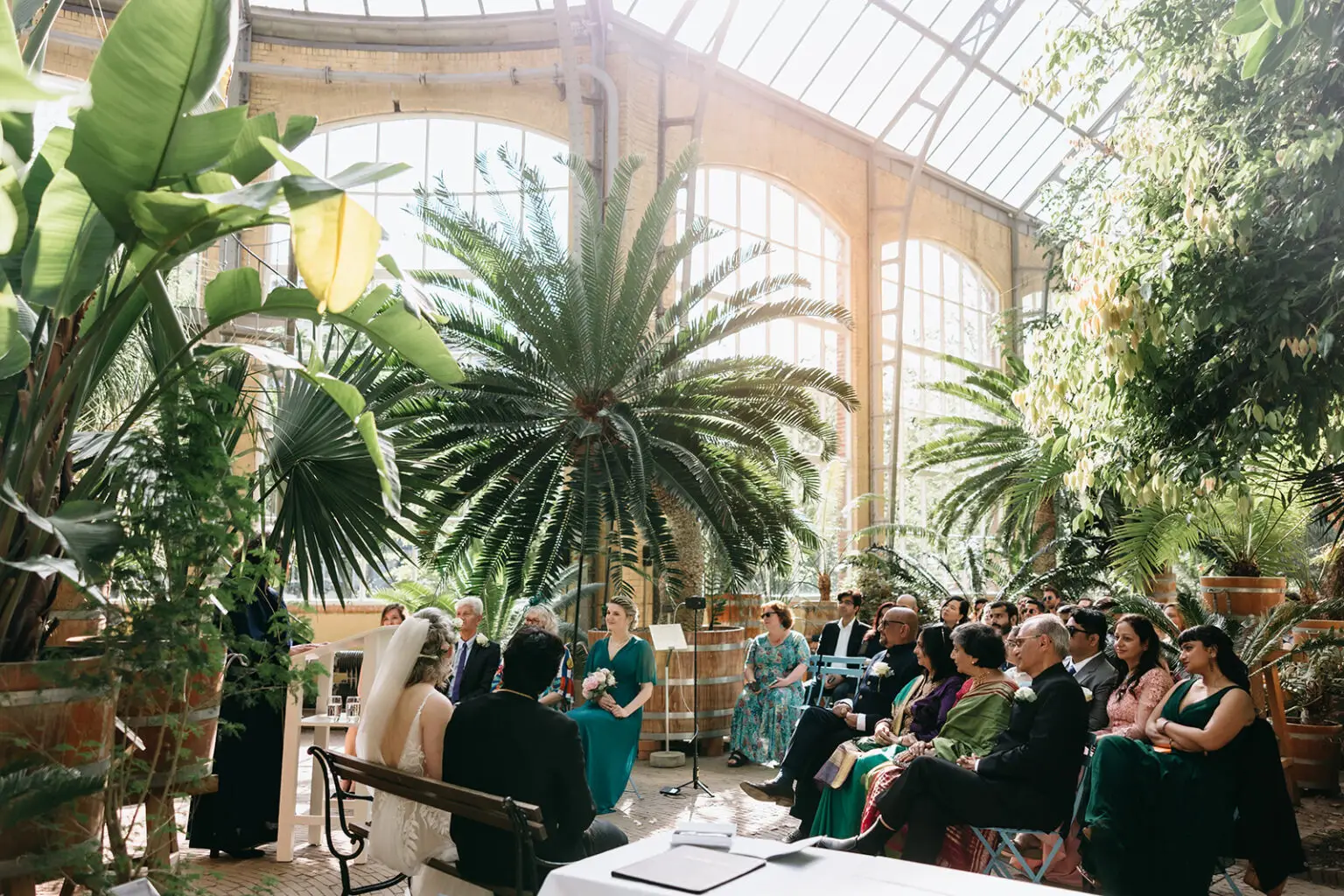 Indoor ceremony inside a greenhouse at Hortus Botanicus Amsterdam with guests surrounded by tropical plants during a wedding at botanical garden Amsterdam