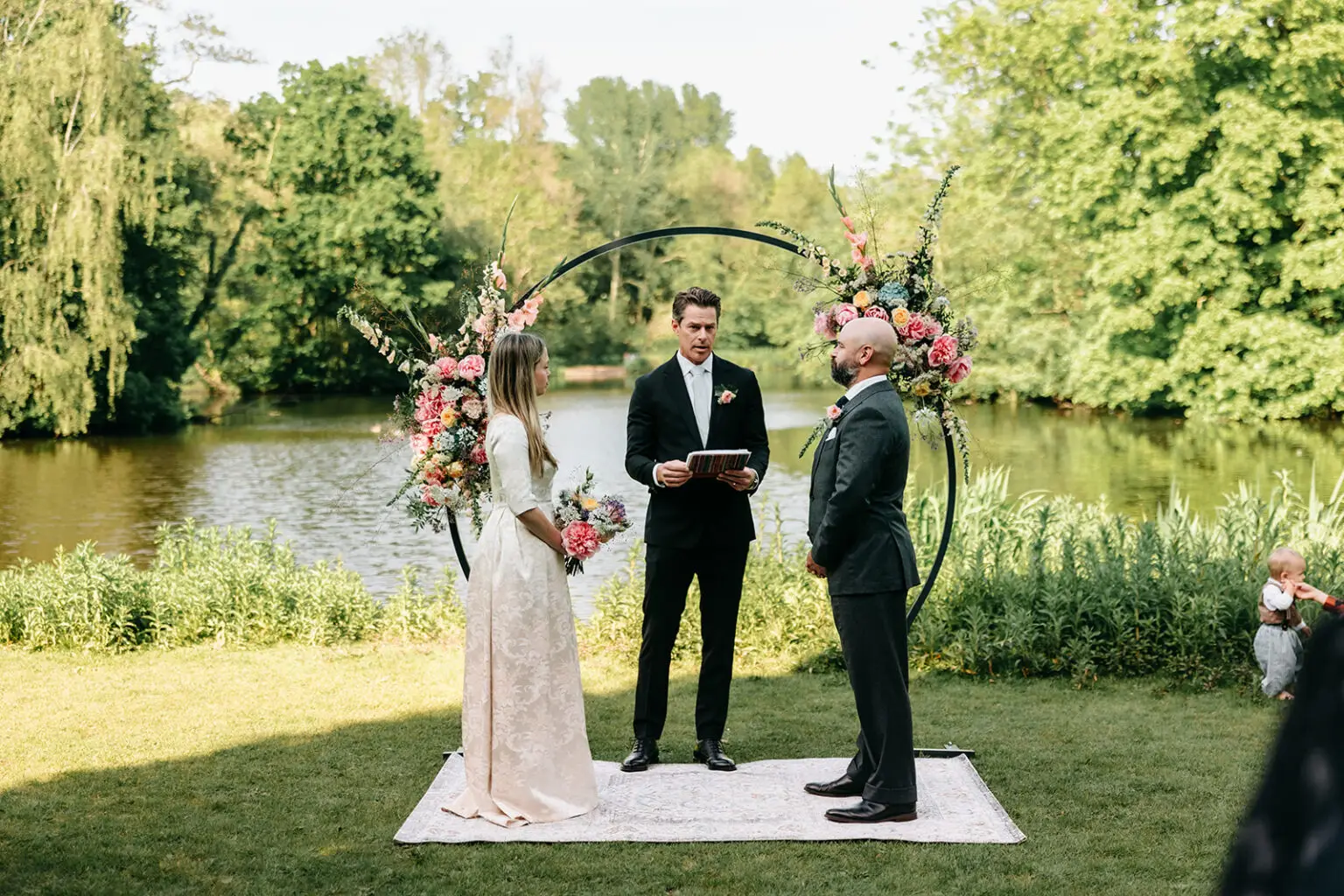 Small outdoor wedding ceremony in a park in Amsterdam with floral arch by the water