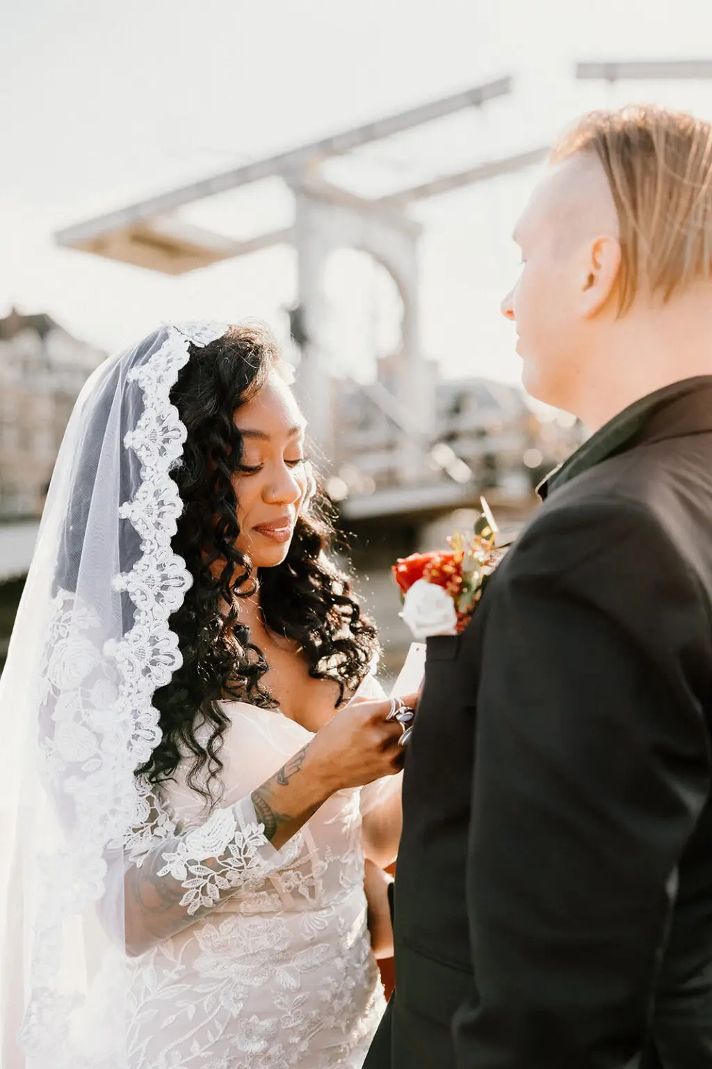 Bride adjusting boutonniere during intimate elopement in Amsterdam with canal bridge in background