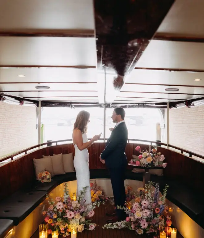 Kristin and Logan exchanging vows inside a flower-filled canal boat during their Amsterdam wedding ceremony
