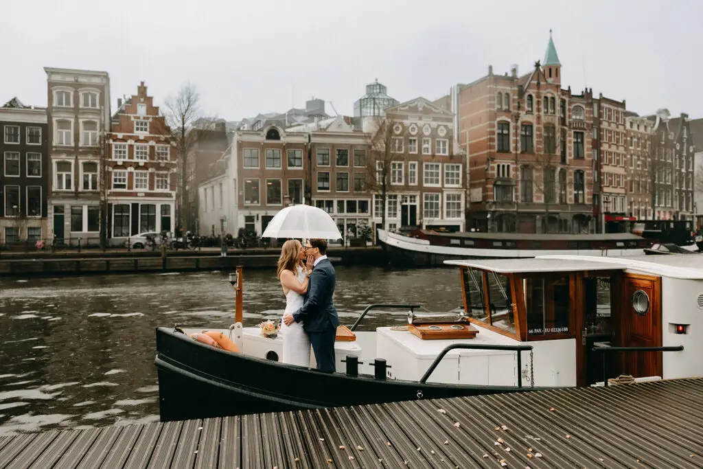 Kristin and Logan kissing under a white umbrella on a canal boat during their March wedding in Amsterdam