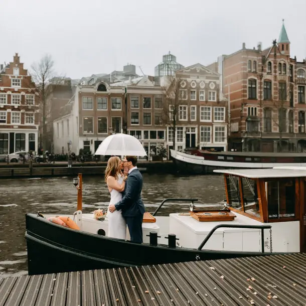 Kristin and Logan kissing under a white umbrella on a canal boat during their March wedding in Amsterdam