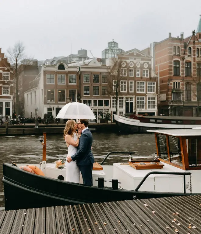 Kristin and Logan kissing under a white umbrella on a canal boat during their March wedding in Amsterdam