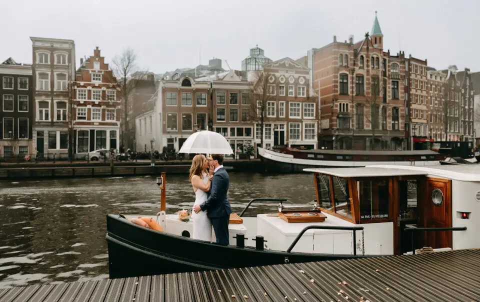 Kristin and Logan kissing under a white umbrella on a canal boat during their March wedding in Amsterdam