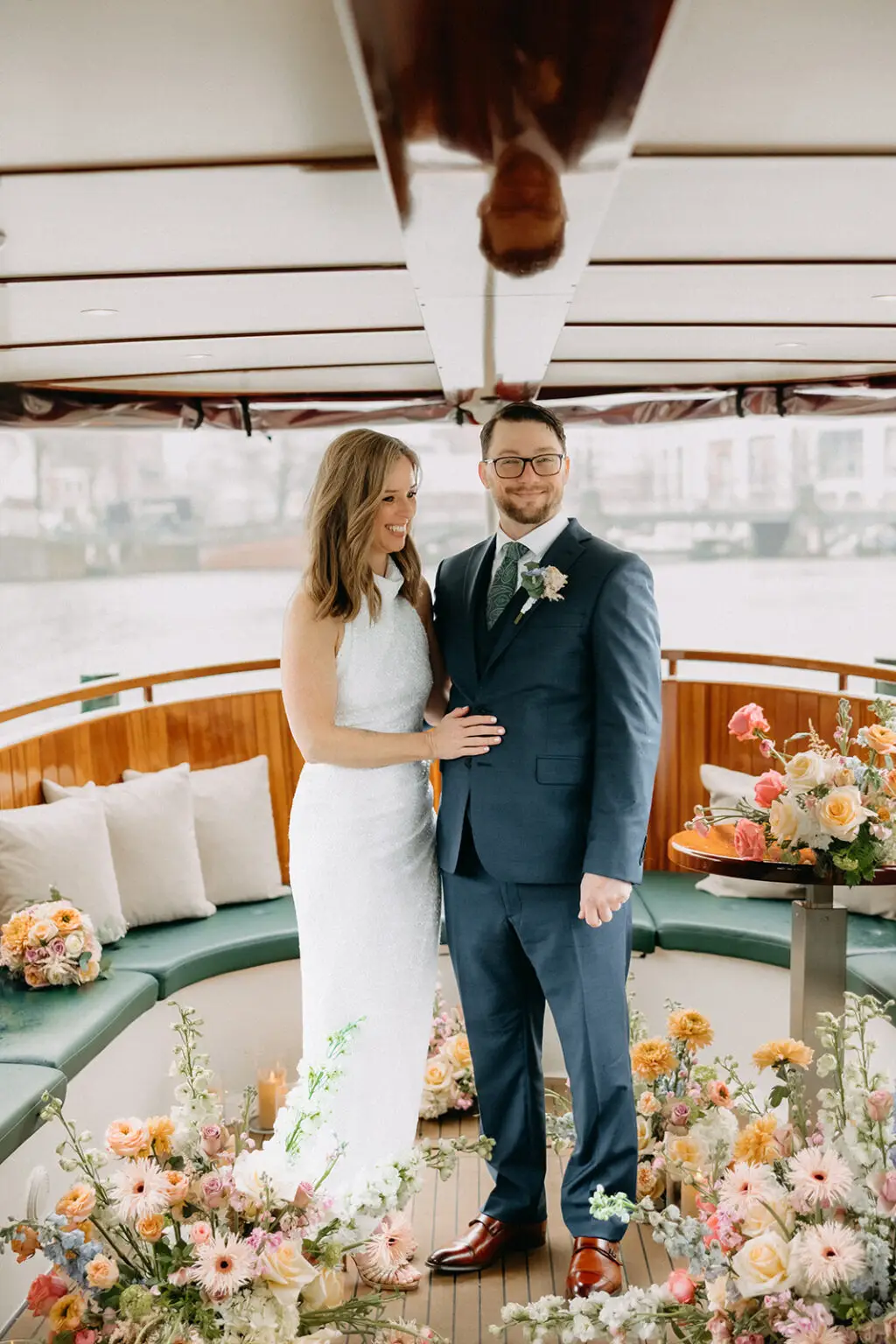 Kristin and Logan standing together inside a private canal boat surrounded by spring wedding flowers in Amsterdam