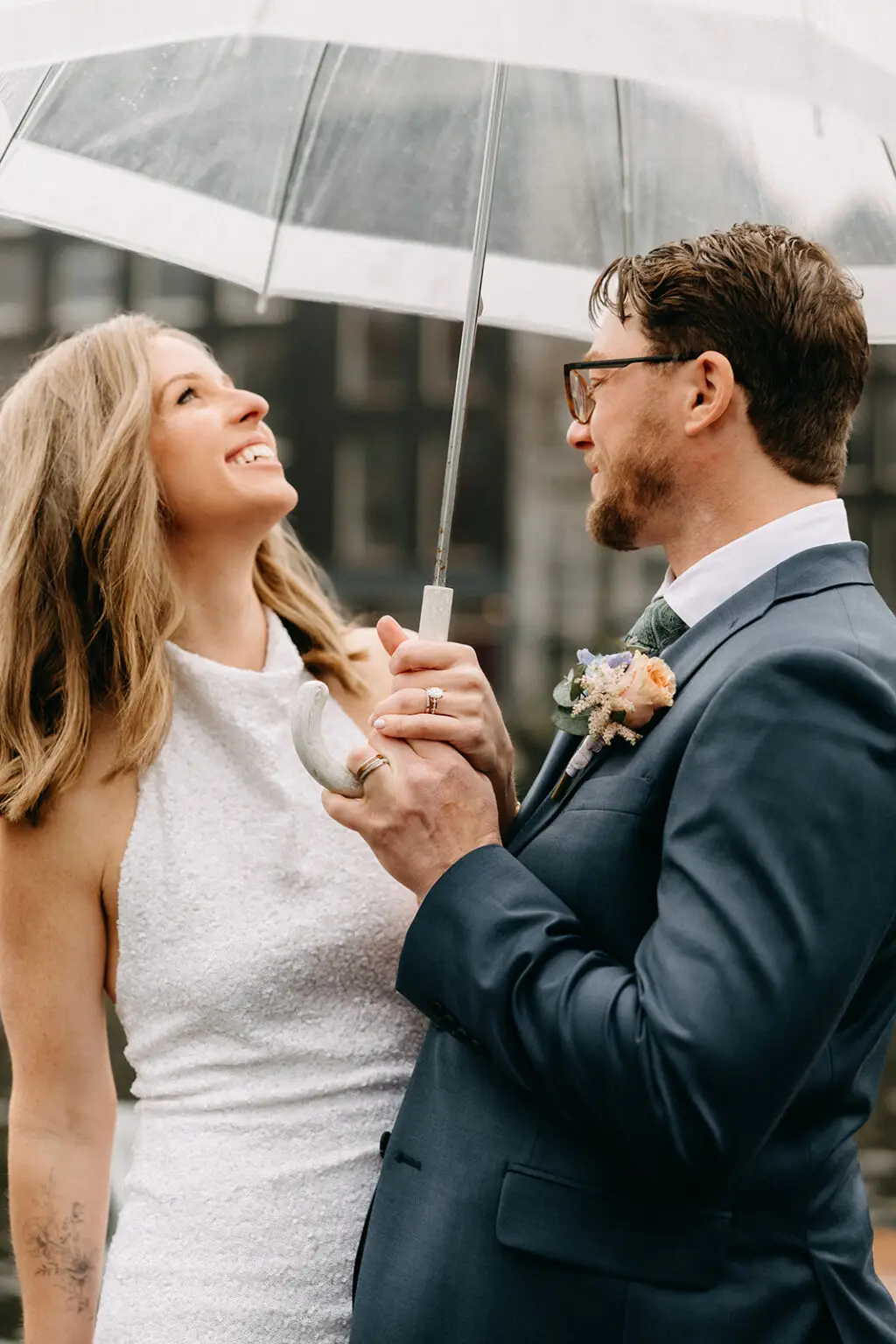 Kristin and Logan smiling at each other under a transparent umbrella during their Amsterdam wedding photoshoot