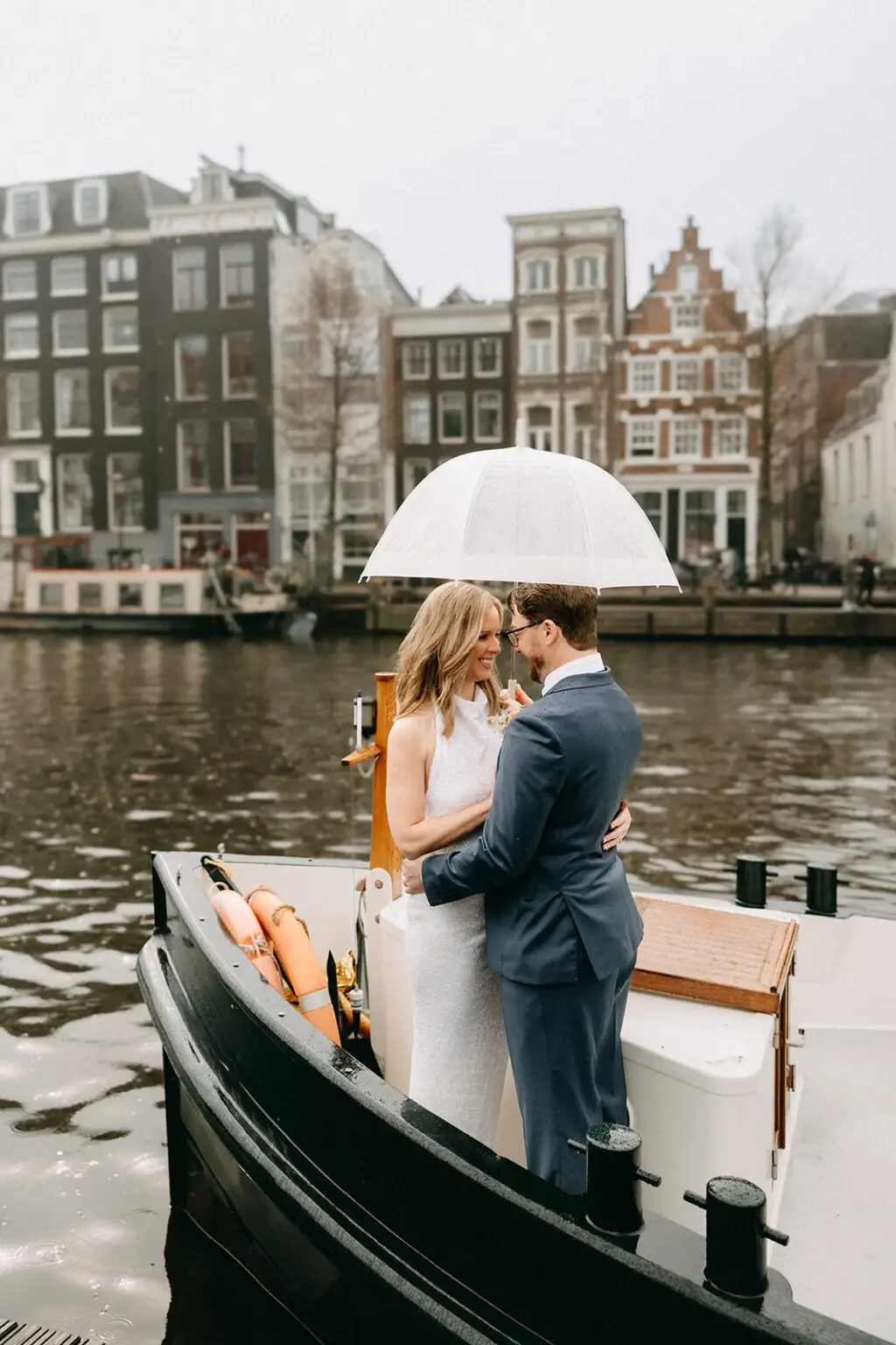 Kristin and Logan embracing under a transparent umbrella aboard their private canal boat in Amsterdam
