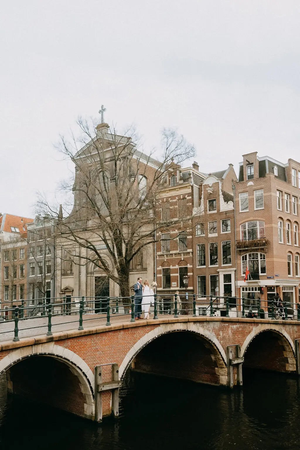 Kristin and Logan standing together on a historic canal bridge during their March wedding in Amsterdam