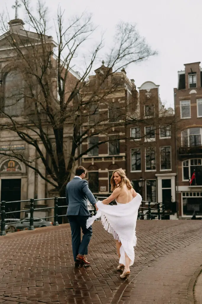 Kristin and Logan walking hand in hand across a historic Amsterdam canal bridge during their wedding photoshoot