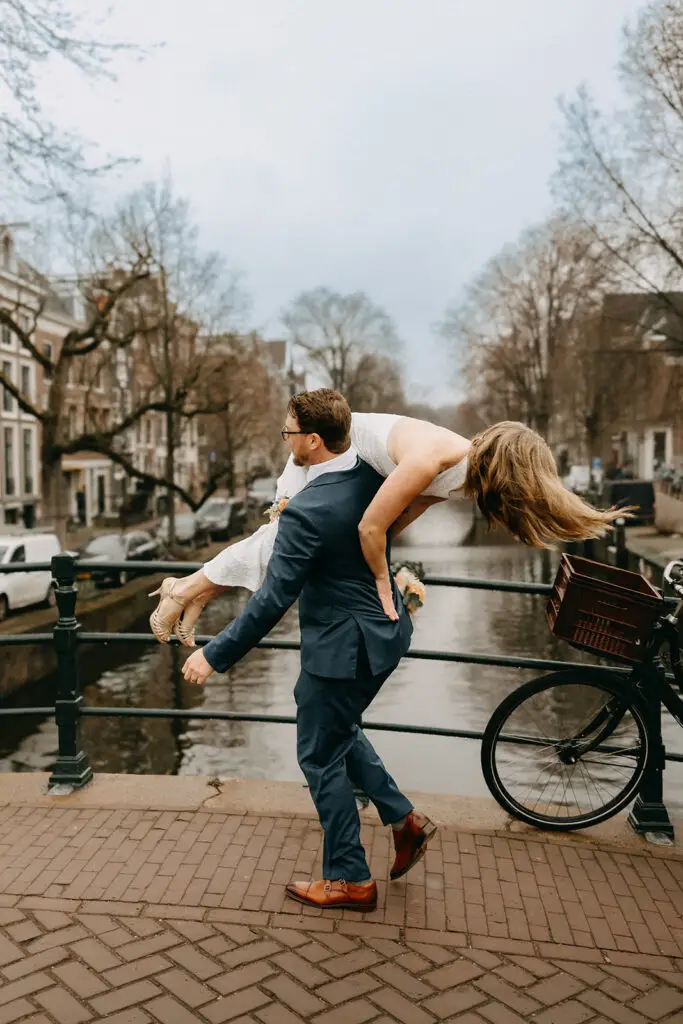 Logan carrying Kristin over his shoulder on a canal bridge during their Amsterdam wedding photoshoot