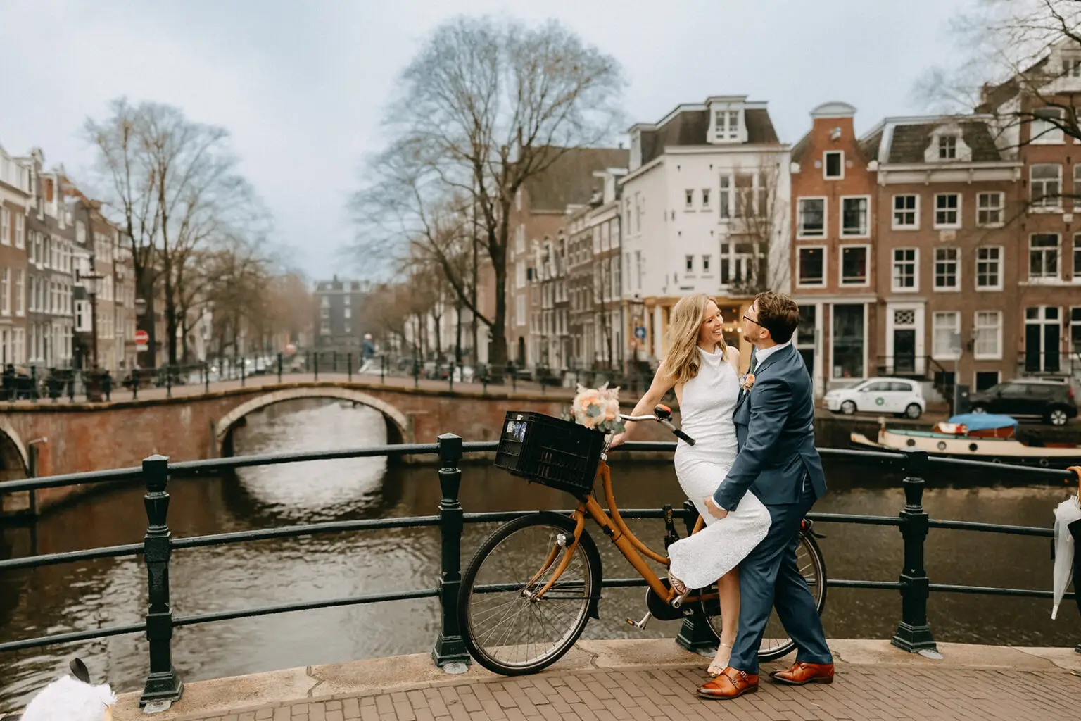 Kristin and Logan posing with a bicycle on a historic Amsterdam canal bridge during their spring wedding photoshoot