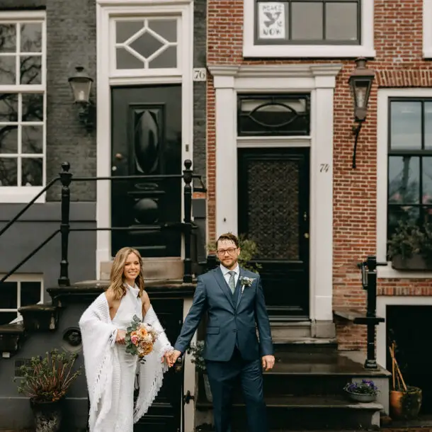Kristin and Logan walking hand in hand along a historic Amsterdam street during their wedding photoshoot
