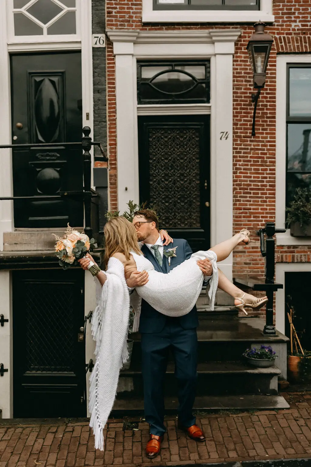 Kristin being carried by Logan in front of traditional Amsterdam canal houses during their wedding photoshoot