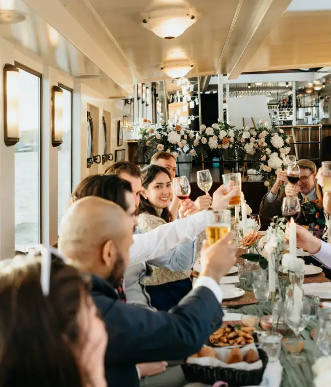 Wedding guests raising glasses together during a destination wedding reception aboard an Amsterdam canal boat
