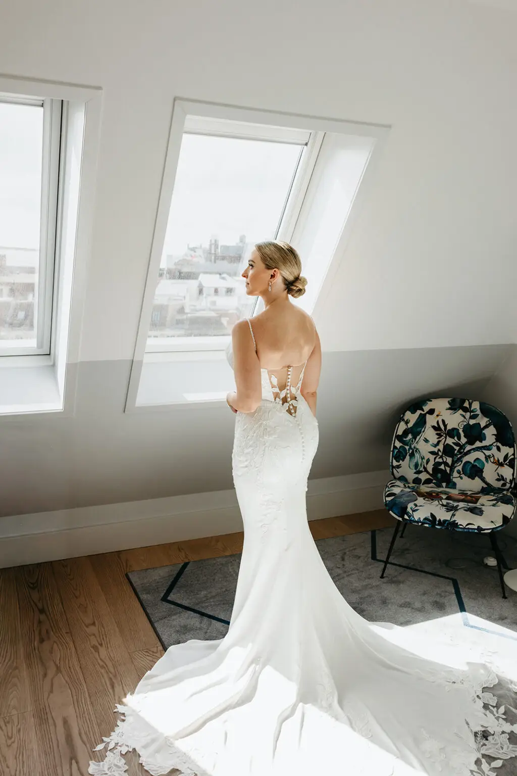 Bride standing beside large windows overlooking Amsterdam during wedding preparations at Hotel De Witt