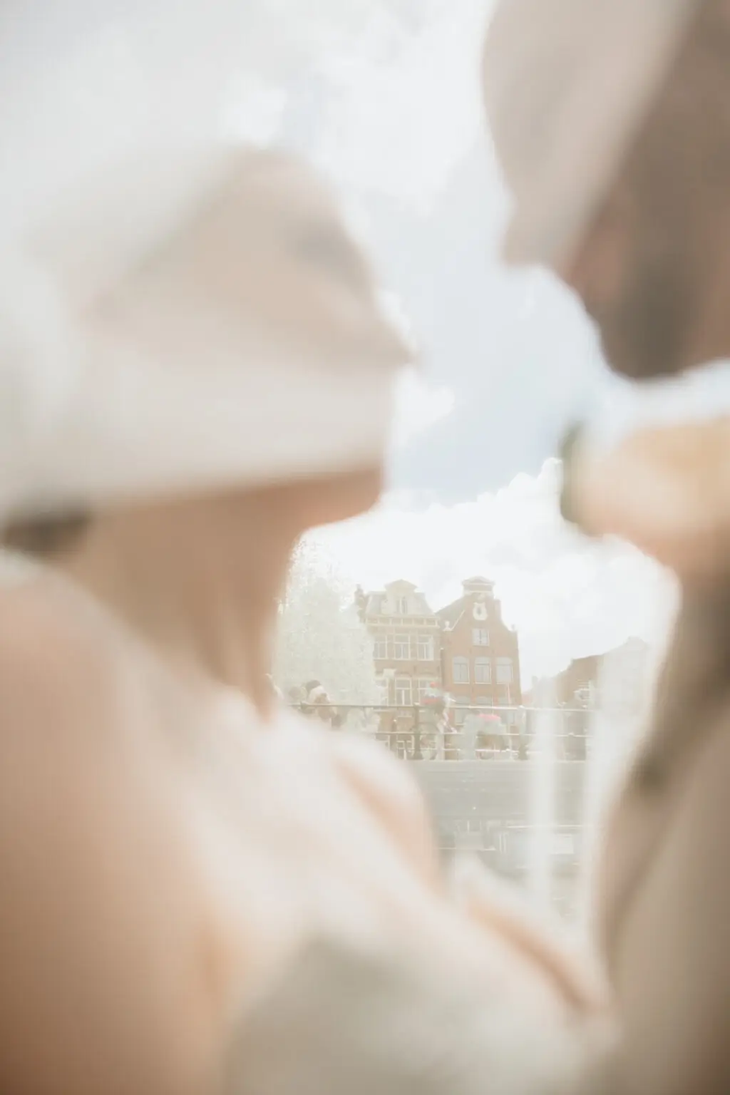 Creative reflection portrait of the bridal couple with historic Amsterdam canal houses softly visible in the background