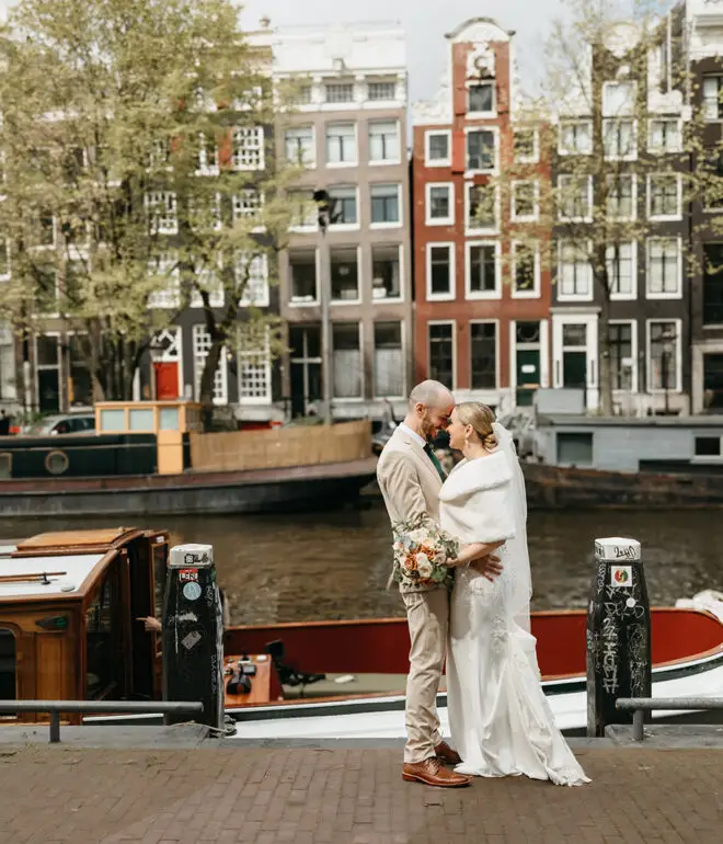 Bride and groom embracing beside Brouwersgracht with historic Amsterdam canal houses behind them