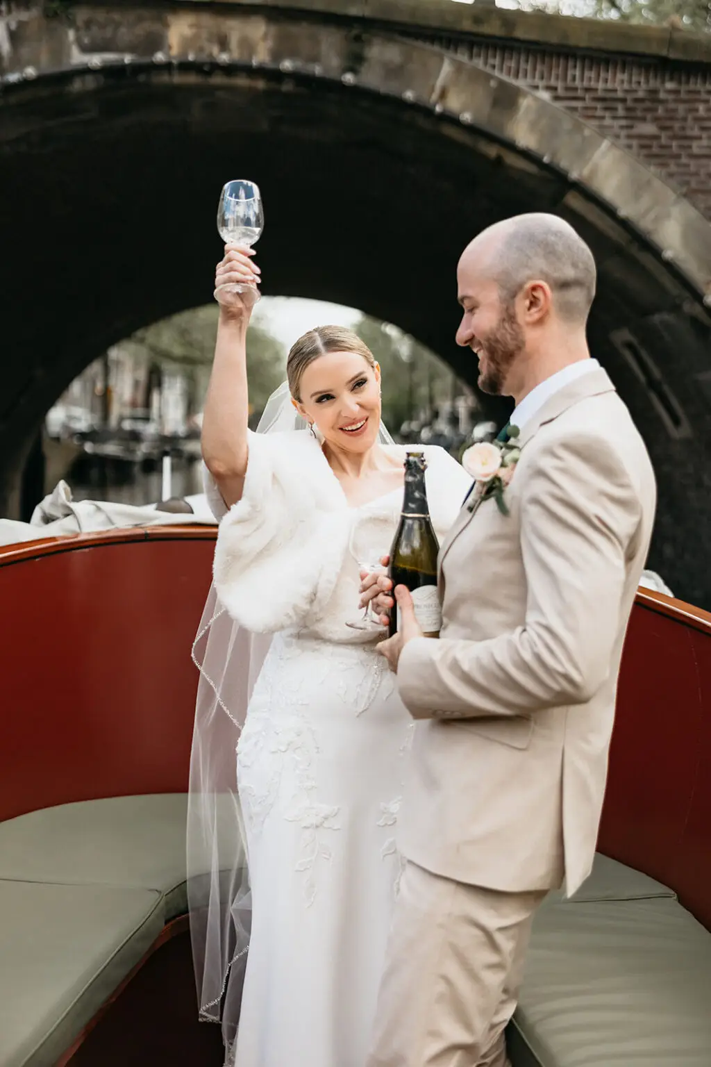 Bride raising a champagne glass beside the groom aboard a wedding boat from Rederij de Nederlanden on the Amsterdam canals.