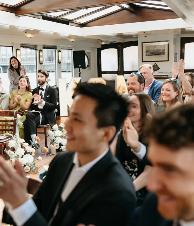 Wedding guests applauding and smiling during a ceremony aboard Het Wapen van Amsterdam