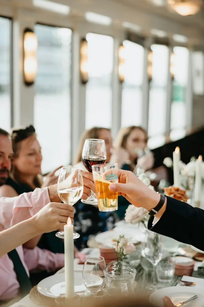 Wedding guests raising glasses in a toast during a destination wedding reception aboard an Amsterdam canal boat