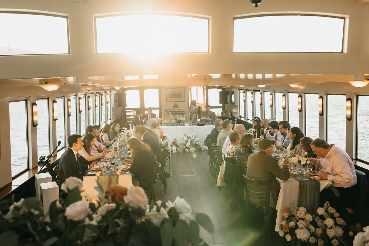 Guests enjoying dinner aboard an Amsterdam canal boat during a destination wedding reception at sunset