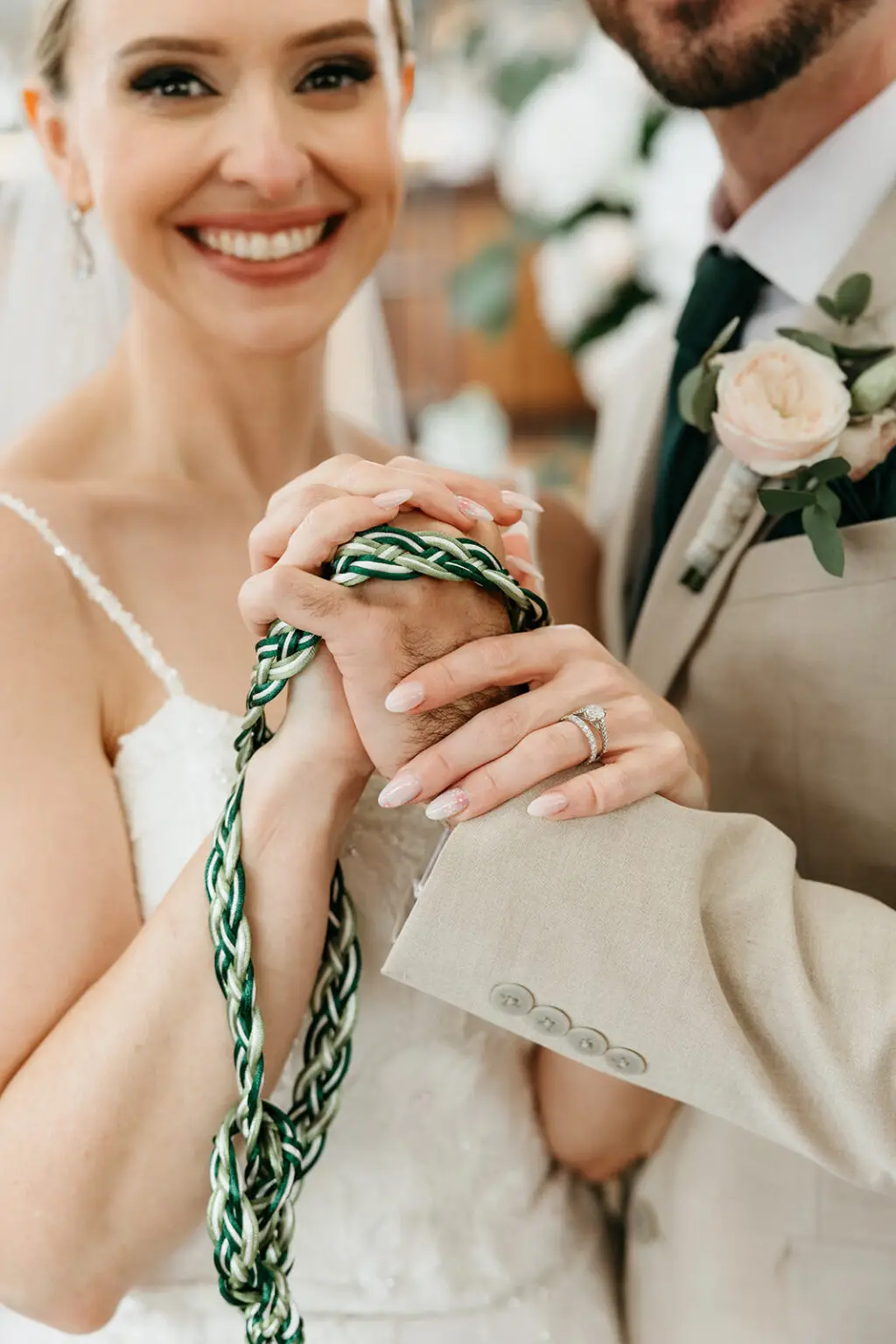 Bride and groom holding hands wrapped in a green handfasting cord during their symbolic wedding ceremony