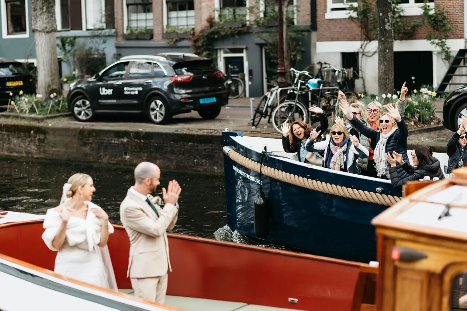 Bride and groom waving to family and friends from their wedding boat on the Amsterdam canals during a celebration with Rederij de Nederlanden.
